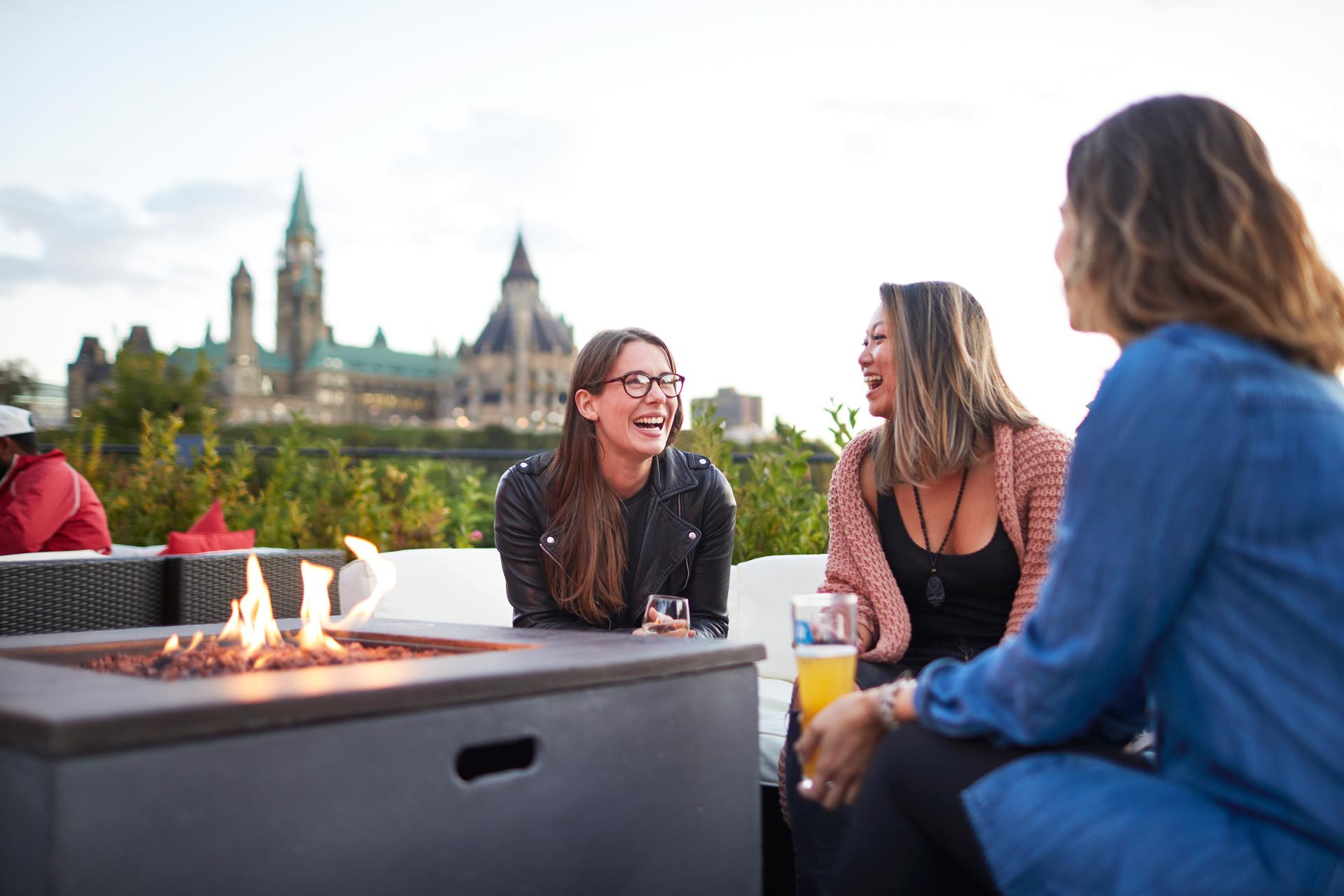 Three people share a drink by a firepit at a tavern near the Ottawa parliament